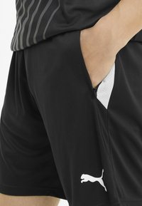 Sorte sportshorts med et elegant design, der har en sidelomme med hvid mesh-foring og et hvidt Puma-logo på kanten.