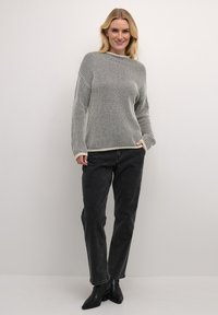 Triibuline pullover, halli ja koorevärvi, pikkade varrukatega ja laia lõikega. Koos kõrge vöökohtadega mustade teksade ning mustade pahklūkkudega saapatega.