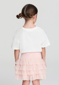 T-shirt bianco a maniche corte in cotone abbinato a una gonna in tulle rosa a strati, con volant e cintura elastica.