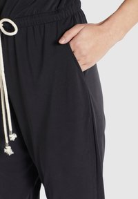 Zwarte joggingsbroek van zacht stof, met een trekkoord in de taille, zijzakken en een relaxte pasvorm. De textuur is glad en flexibel.