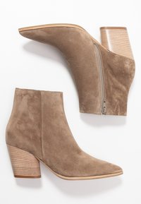 Suedepohjaiset nilkkurit vaaleanruskeana, joissa on terävä nenä, paksu puun näköinen korko ja sivuvetoketju helppoa päällepantavuutta varten.