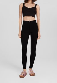 Musta lyhythihainen toppi paksuilla olkaimilla, yhdistettynä korkeavyötäröisiin mustiin legginsseihin ja vaaleanpunaisiin platform-sandaaleihin, joissa on kaksi solkea. Sileä pinta.