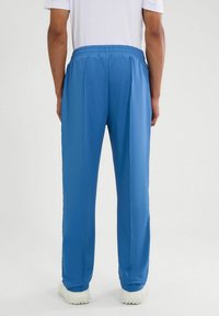 Jasnoniebieskie spodnie sportowe z elastycznym paskiem w talii, o gładkiej teksturze i zwężających się nogawkach, pokazane od tyłu.