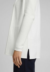 Bílý dlouhý rukáv top s texturovaným povrchem, s bočními rozparky, spadlými rameny a volným střihem. Hladká tkanina.