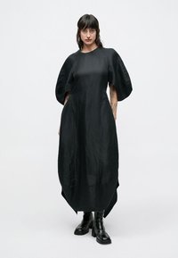 Μαύρο φόρεμα μήκους μέχρι το γόνατο με χαλαρή, δομημένη σιλουέτα και υπερμεγέθη μανίκια. Κατασκευασμένο από λείο, υφασμάτινο ύφασμα με υφή.