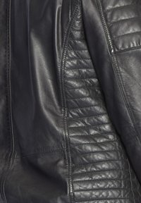 Schwarze Lederjacke mit glatten und strukturierten Paneelen, versehen mit gesteppten Akzenten an den Schultern und an der Seite. Maßgeschneiderter Schnitt mit genähten Nähten.