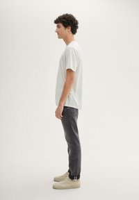 Light gray short-sleeve t-shirt, dark gray slim-fit jeans, and beige sneakers, shown from the side against a neutral background.