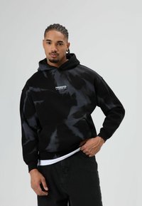 Zwart tie-dye hoodie met een voorzak, met witte tekst "PRESENTED". Gemaakt van een zachte stof, met lange mouwen en een losse pasvorm.