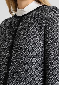 Svart och grå stickad cardigan med ett diamantmönster, rund halsringning och knappstängning fram.