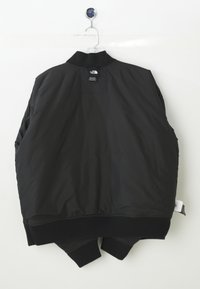 Veste bomber noire, bouffante, avec un col et des poignets en côte. Présente une étiquette à l'arrière et une texture de tissu lisse et brillant.