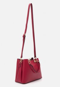 Sac à main en cuir rouge au design structuré, avec des accents en métal doré, une bandoulière amovible et deux anses supérieures.