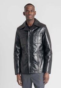 Zwarte leren jas met een kraaghalslijn, voorzien van twee voorkleppen en knoopsluitingen, gladde textuur en een getailleerde pasvorm.