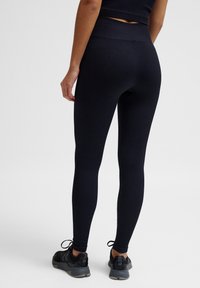 Schwarze gerippte Leggings mit hohem Bund und figurnaher Passform. Getragen mit schwarzen Sportschuhen, die Schnürsenkel und eine strukturierte Oberseite haben.
