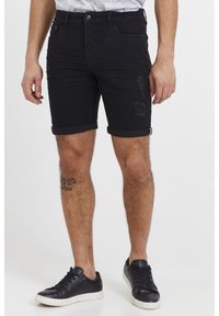 Mustad teksapüksid, mille ääred on üles keeratud, kaunistatud kulunud detailidega ja ees nupuga kinnitatavad. Sobitatud mustade tennistega.