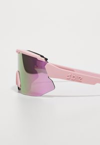 Rosa sportsolbriller med en stor, buet, gradient lilla linse og sorte accenter på rammen, med en teksturert grep på nesebroen.