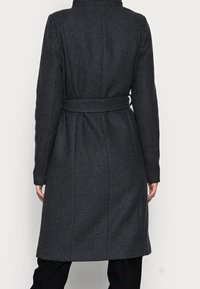 Cappotto di lana grigio scuro con vita aderente, maniche lunghe e silhouette dritta; presenta un alto colletto e dettagli sulle cuciture sul retro.