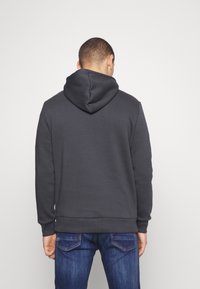 Sudadera gris oscuro con una gran capucha redonda y puños de canalé. Tejido suave con una textura lisa, combinada con unos vaqueros de mezclilla azul.