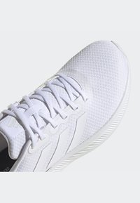 Scarpa sportiva bianca con tomaia in mesh testurizzato, lacci piatti e tre strisce distintive sul lato; presenta una suola bianca liscia.
