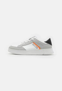 Sneaker grigia e bianca con sopra in pelle liscia, accentuazione arancione, dettagli perforati e suola in gomma. Presenta lacci e logo sul lato.