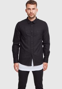 Camisa negra de botones hecha de un tejido texturizado. Presenta dos bolsillos en el pecho, mangas largas y un cuello clásico.