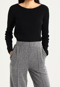 Pull-over noir côtelé à manches longues avec un col large, assorti à un pantalon gris texturé taille haute avec plis devant et poches latérales.