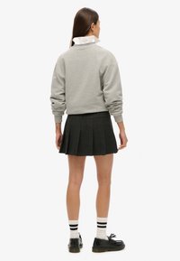 Grijze sweatshirt, geplooide zwarte rok, witte bloes eronder, donkere schoenen en gestreepte sokken. Textuur en casual ensemble.