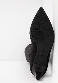 Botte noire à bout pointu avec une tige d'aspect satinée et un talon incurvé. La semelle présente des motifs embossés et le nom de la marque "KAISER".