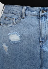 Světle modrá džínová sukně s třepícími se detaily na přední straně. Obsahuje klasický pětiboxový design a vysoký pas.