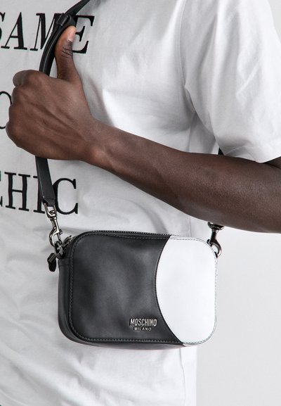 Black and white leather crossbody bag with a rounded design, silver hardware, and embossed "Moschino Milano" logo on the front.
