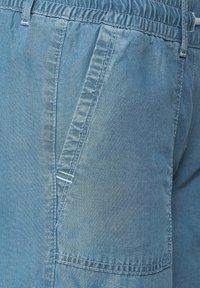 Pantalones cortos de mezclilla azul claro con cintura elástica, que cuentan con un bolsillo delantero con costuras verdes y una textura suave, ligeramente desgastada.