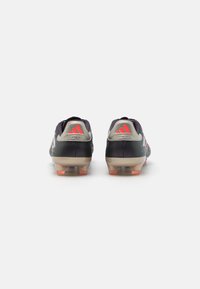 Scarpe da football nere con accenti argentati. Presentano un logo rosso e tre strisce. Materiale testurizzato con suola sagomata e tacchetti rimovibili.