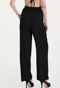 Pantaloni neri a gamba larga con vita elastica, texture liscia e vestibilità ampia. Presentano una vita alta e un design a lunghezza completa.