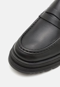 Mocassins en cuir noir avec une finition lisse, des coutures discrètes, un bout arrondi et une semelle en caoutchouc texturée pour une meilleure adhérence.
