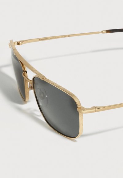 Γυαλιά ηλίου τύπου aviator με μεταλλικό πλαίσιο σε χρυσό χρώμα, σκούρους φακούς και διακριτικό χαραγμένο σχέδιο στις άκρες του πλαισίου.