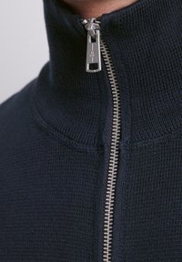 Maglione con zip di colore blu navy, dotato di collo alto, con una zip argentata e tessuto testurizzato, che sottolinea una finitura liscia e una vestibilità aderente.