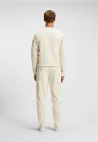 Beige sportieve sweatshirt met lange mouwen, voorzien van uitsnijdingen; gecombineerd met bijpassende taps toelopende sweatpants. Soepele stof textuur.