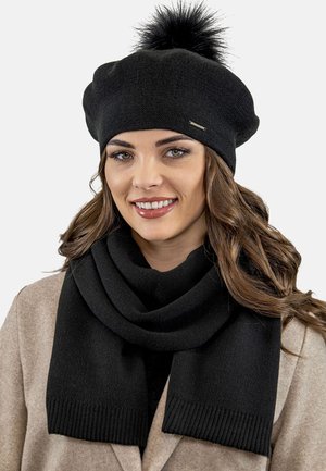 Beret negru din tricot cu o pompom din blană sintetică, asociat cu o eșarfă neagră asortată. Ambele articole au o textură în lurex și un material moale.