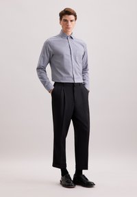 Camicia a quadri blu e bianca, abbinata a pantaloni neri a pieghe e scarpe stringate nere. Tessuto liscio e vestibilità su misura.