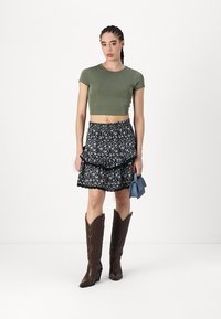 Oliven grønn cropped t-skjorte, lagdelt marineblå blomsterkjole med blå og hvite blomster, og brune cowboy støvler med teksturerte detaljer.