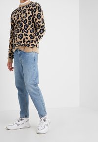 Leopardmönstrad tröja i brunt och svart, parat med ljusblå raka jeans och vita sneakers med grå detaljer.