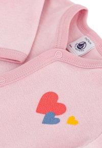 Rosa Babystrampler mit weichem Material, der drei bunte Herzdesigns in Rot, Blau und Gelb zeigt. Druckknopfverschluss am Ausschnitt.