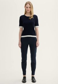 Tengerészkék bordázott kötött felső rövid ujjakkal és kontrasztos fehér mandzsettával, karcsúsított tengerészkék nadrággal és fekete fűzős cipővel párosítva.