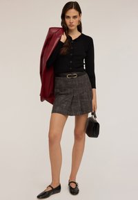 Svart ribbad knäpptröja, grå rutig kort kjol med en guldfärgad bältesspänne, i kombination med svarta skor och en strukturerad svart handväska. Röd jacka hängande.