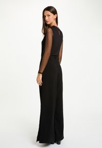 Mono negro con mangas largas de tul con lunares y un discreto escote en la espalda. Pantalones acampanados con un ajuste a medida y tejido texturizado.