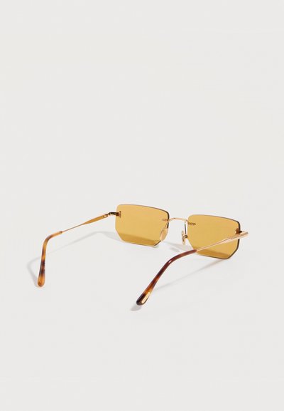 Ορθογώνια γυαλιά ηλίου με κεχριμπαρένιο τόνο, λεπτά χρυσά μεταλλικά πλαίσια και καμπυλωτά ακουστικά με μοτίβο χελώνας, ακουμπισμένα σε λευκή επιφάνεια.