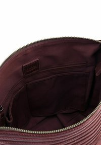 Interno di borsa in pelle bordeaux con esterno testurizzato, chiusura con zip e fodera in tessuto che presenta una tasca con zip e due tasche aperte.