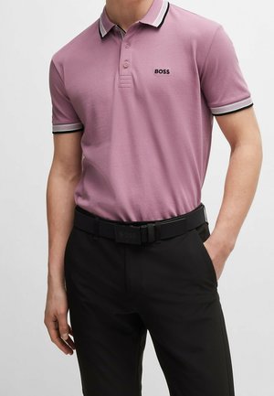 Muž v lila polotriku s bílým a černým lemováním a logem BOSS, zastrčený do černých kalhot s černým pásem.