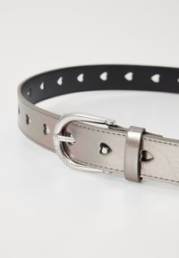 Cinturón metálico plateado con recortes en forma de corazón, que presenta una hebilla plateada brillante y una textura suave. El interior es negro.