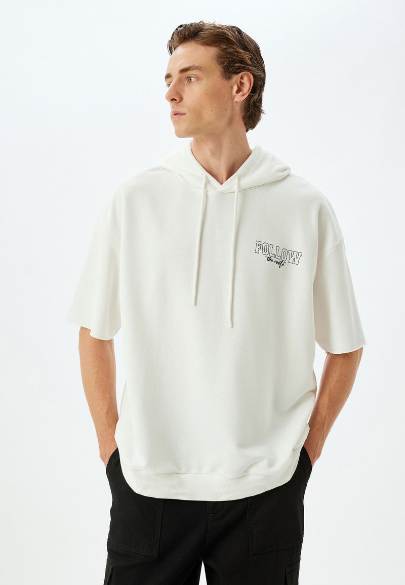 Witte hoodie met korte mouwen en een verstelbare capuchon. Voorzien van een kleine geprinte "FOLLOW" tekst op de borst. Zacht materiaal en een comfortabele pasvorm.