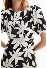 Blumenkleid mit schwarzem Hintergrund und großen weißen Blumenmustern, kurzen Puffärmeln und einem enganliegenden Oberteil mit glatter Textur.